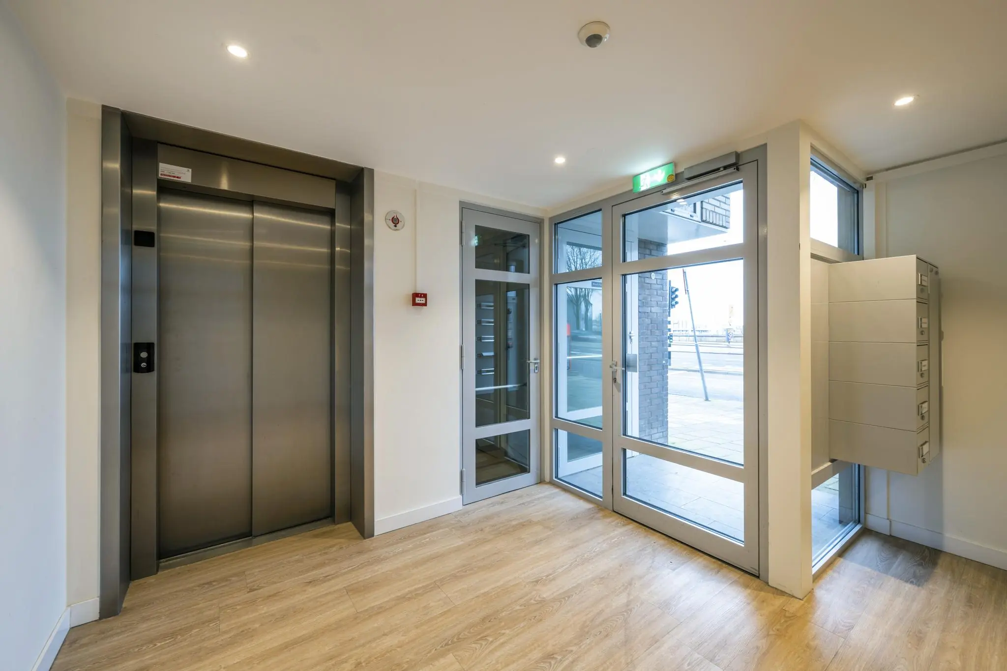 Ingang van een modern appartementencomplex aan de Prins Hendrikkade met lift, brievenbussen en glazen toegangsdeuren.